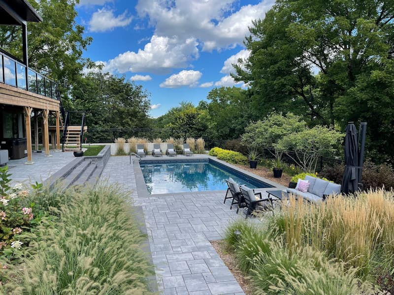 An inground pool that has been installed in a backyard with a stone patio and gardens.
