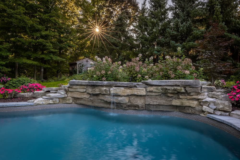  Alt text: A custom pool waterfall next to an inground pool, surrounded by a garden.